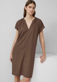 Robe en lin marron avec des manches courtes évasées, décolleté en V et coutures verticales discrètes. Texture douce et longueur au genou.