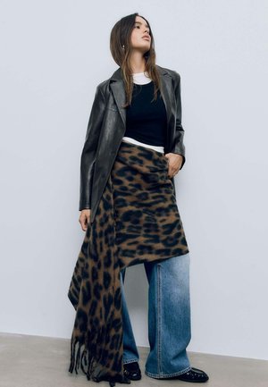 Schwarze Lederblazer, figurbetontes schwarzes Oberteil, braßer Leopardenmuster Schal um weit geschnittene Jeans und schwarze Schuhe mit strukturierter Oberfläche.