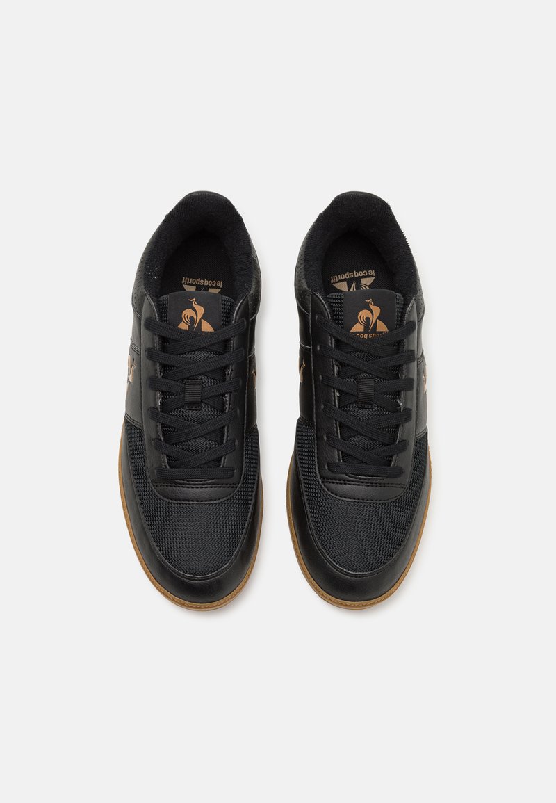 Zapatillas negras que presentan una combinación de cuero suave y textura de malla, con cordones redondos, una suela de goma y un detalle de logo en la lengüeta.