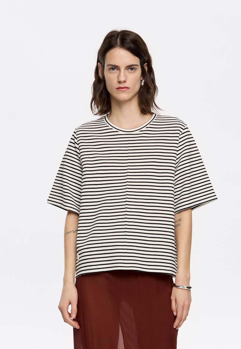T-shirt à manches courtes rayé en mélange de coton beige et noir, avec un col rond et une coupe décontractée. Accompagné d'une jupe en tulle bordeaux.