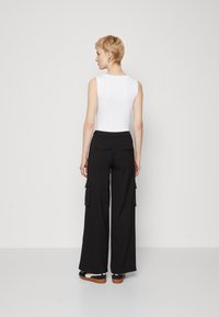 White sleeveless top paired with black wide-leg cargo pants, featuring two large side pockets and a smooth fabric texture.