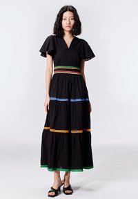 Robe maxi en coton noir avec des manches courtes à volants, décolleté en V, et des accents en crochet colorés en orange, vert, bleu et rose.
