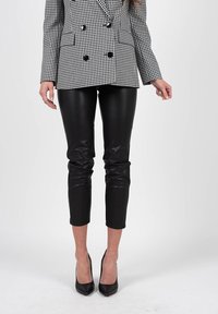 Blazer à carreaux noir et blanc à double boutonnage avec de gros boutons, associé à un pantalon en cuir noir ajusté et des escarpins noirs à talons pointus.