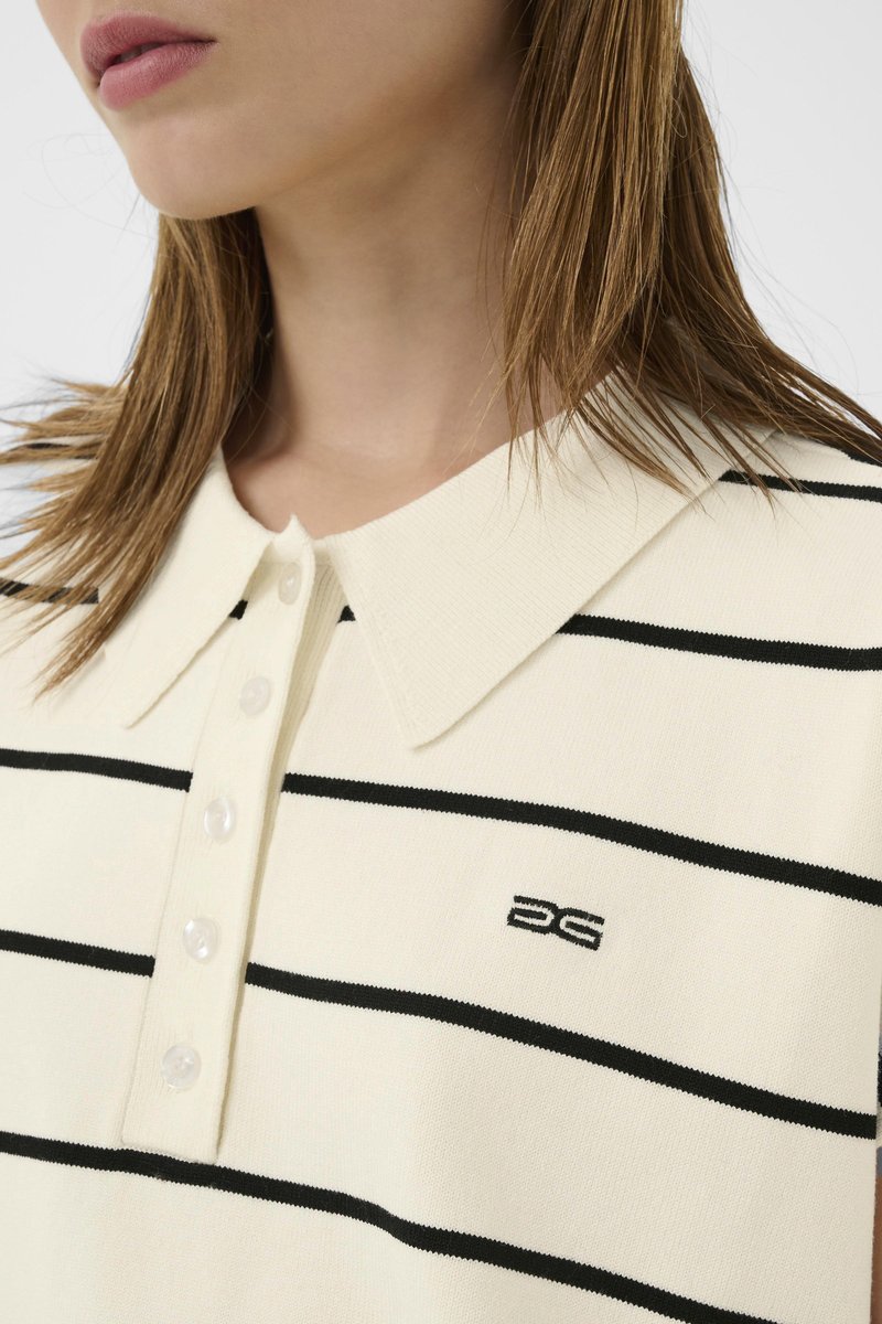 Kvinde iført cremefarvet, kortærmet poloshirt med sorte vandrette striber og et lille sort broderet logo på brystet.