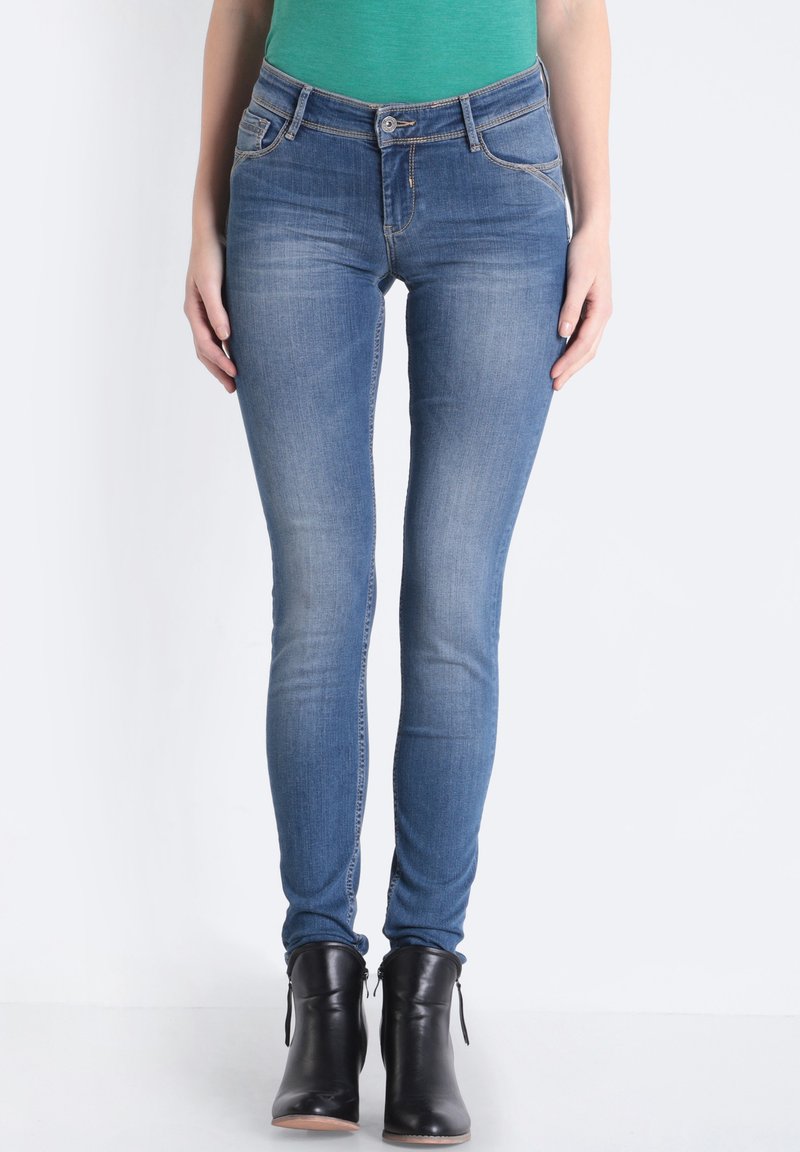 Vaqueros ajustados de denim azul claro, con un diseño clásico de cinco bolsillos, lavado desgastado y costuras sutiles. Combinados con botas negras de tobillo.