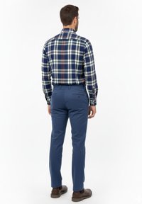 Camisa de cuadros para hombre en tonos azul marino, blanco y naranja, combinada con pantalones azules. La camisa cuenta con un cuello abotonado y mangas largas.