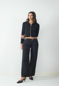 Zwarte cropped zip-up top met lange mouwen, gecombineerd met zwart hoge taille wijde broek en zwarte puntige slingback schoenen.