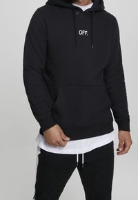 Svart huvtröja i bomullsblandning, med en framficka som en känguru, dragsko i huvan och vit "OFF." text på bröstet.