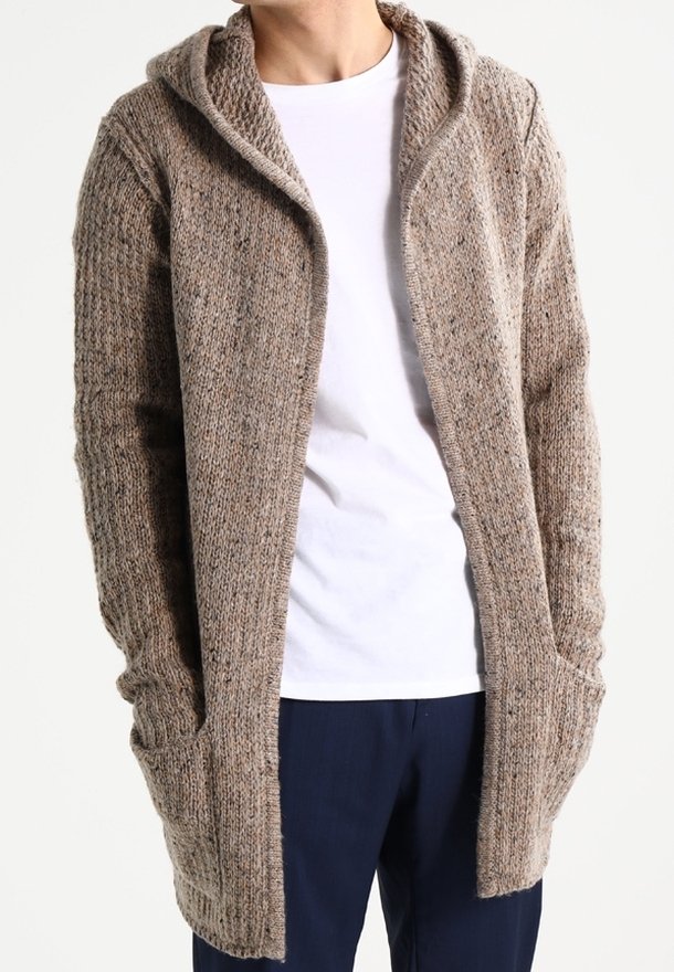 Cardigan lungo aperto sul fronte in maglia testurizzata color marrone chiaro. Dotato di cappuccio e tasche laterali. Indossato sopra una camicia bianca e pantaloni scuri.