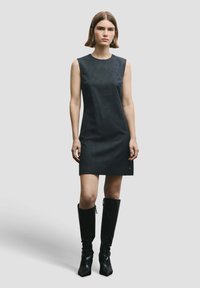 Abito nero senza maniche con trama a righe verticali, lunghezza al ginocchio, abbinato a stivali neri alti e lucidi con punta quadrata.