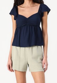 Navy blue short-sleeve top with gathered center, flared hem, paired with light beige shorts. Soft fabric, relaxed fit, minimal design.