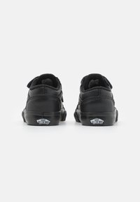 Baskets en cuir noir avec surface texturée, design bas et bandes Velcro. Présente un logo sur le talon et une semelle en caoutchouc durable.