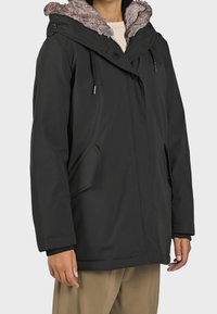 Svart isolerad jacka med huva i fuskpäls, med framknappstängning, justerbara dragsko och två sidofickor.