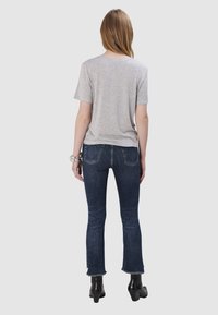 T-shirt gris à manches courtes associé à un jean évasé bleu marine, avec un ourlet effiloché et une texture usée, porté avec des bottines noires.