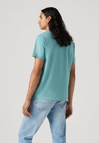 Turkis bluse med korte ærmer lavet af blødt stof, med en lige pasform og en ren rund halsudskæring, parret med lyseblå jeans.