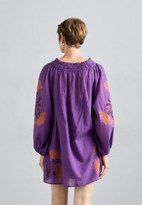 Robe violette ample avec des manches longues, ornée de motifs floraux orange sur les manches et l'ourlet, et avec un encolure élastique.