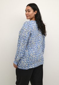 Blusa blu a maniche lunghe con motivo astratto di foglie in bianco e blu scuro. Tessuto morbido e fluido con una vestibilità comoda e scollo rotondo.