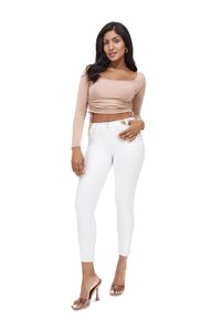 Top court beige à manches longues avec détail à cordon, associé à un pantalon skinny blanc taille haute, complété par des sandales à talons transparents.