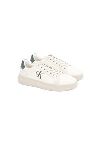 Zapatillas de cuero blancas con suela de goma texturizada, que presentan un acento verde en el talón y un logo en el lateral. Cuerdas planas.