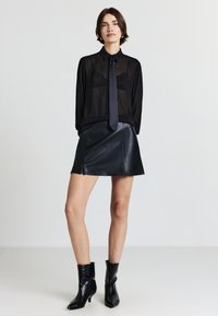 Camicia nera trasparente con bottoni e colletto, abbinata a una mini gonna in pelle nera. Stivaletti neri lucidi con punta a forma di cono.