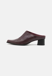 Mules de cuero burdeos con punta ligeramente afilada y tacón bloque de altura media. Textura suave y diseño minimalista sin herrajes visibles.