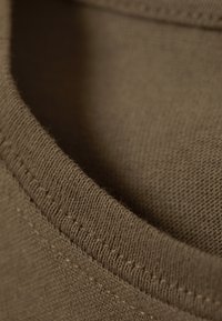 Material maro cu un guler cu nervuri, evidențiind o textură moale și cusături vizibile. Materialul pare ușor și elastic.