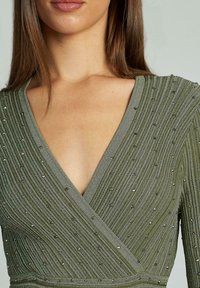 Rochie verde învelitoare dintr-un material texturat, având nervuri verticale și aplicații metalice răspândite pe decolteu și bust.