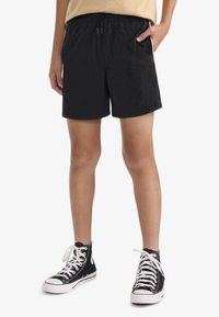 Shorts noirs avec une taille élastique et un cordon de serrage, dotés d'un design à bande latérale. Associés à des baskets montantes noires avec des lacets blancs.