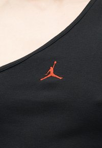 Κοντινό πλάνο μαύρου ριγωτού τοπ χωρίς μανίκια με πορτοκαλί κεντητό λογότυπο παίκτη μπάσκετ κοντά στη λαιμόκοψη.