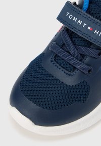 Granatowy but sportowy z siateczkowej tkaniny, błyszczącymi akcentami i białą gumową podeszwą. Zawiera rzep z detalem logo oraz sznurowadła.