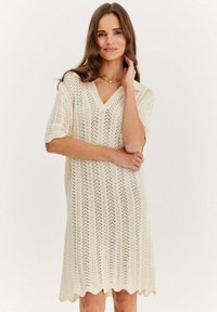 Sukienka dzianinowa w kolorze kremowym, z dekoltem w kształcie litery V, krótkimi rękawami oraz fakturowanym, ażurowym wzorem z falbanowym wykończeniem dołu.