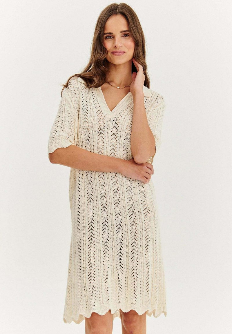 Sukienka dzianinowa w kolorze kremowym, z dekoltem w kształcie litery V, krótkimi rękawami oraz fakturowanym, ażurowym wzorem z falbanowym wykończeniem dołu.