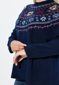Granatowy sweter z teksturowanym wzorem dzianinowym z kolorowymi motywami, w tym niedźwiedziami, płatkami śniegu i dekoracyjnymi akcentami na karczku.