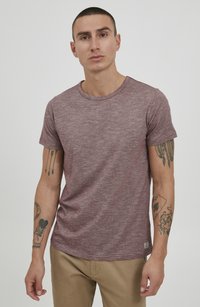 Kortermet maroon teksturert T-skjorte med rund hals og liten logoetikett på kanten, brukt med lyse beige bukser.