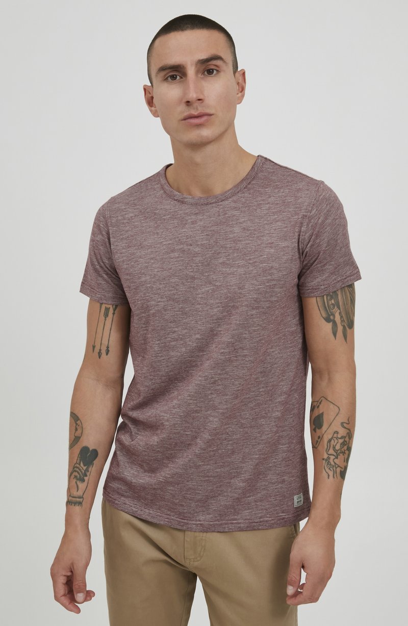 Kortermet maroon teksturert T-skjorte med rund hals og liten logoetikett på kanten, brukt med lyse beige bukser.