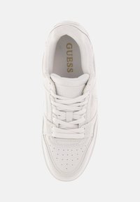 Sneaker bianca con punta perforata, pannelli laterali testurizzati e collo imbottito. Logo "GUESS" impresso in oro sulla linguetta.