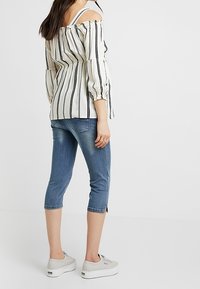 Vit och svart randig off-shoulder topp med puffärmar, parat med korta blå denimjeans och ljusgrå plattformsneakers.