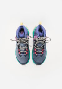 Multicolored sports shoes with a dark blue upper, gray laces, green and purple accents, padded collar, and textured rubber sole.