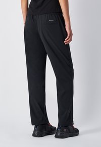 Zwarte sportbroek met een elastische tailleband, achterzak, gladde textuur en zijnaad. Gecombineerd met zwart-rode sneakers.