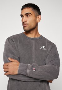 Gray sweatshirt made of cotton blend, featuring a round neckline, long sleeves, and embroidered Champion logo on chest and cuff.