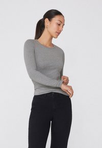Graues langärmliges T-Shirt aus weichem Stoff, mit rundem Ausschnitt, figurbetonter Silhouette und glatter Textur, kombiniert mit schwarzen Jeans.