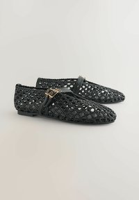 Schwarze gewebte Loafer aus flexiblem Material mit strukturiertem Oberflächen. Besitzt einen Riemen mit dekorativer Hardware in Goldtone.