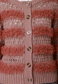 Πλεκτή ζακέτα σε απαλό ροζ, με υφασμάτινες κοραλί ρίγες. Στρογγυλή λαιμόκοψη με πέντε κουμπιά. Ανοικτό πλέξιμο με ριμπ τελείωμα και μανσέτες.