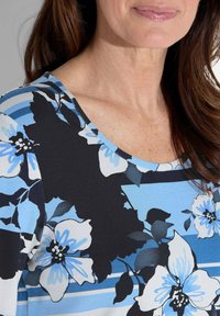 Floral top met een zwart en blauw ontwerp met grote witte bloemen. Ronde halslijn, zachte stof en horizontale strepen in verschillende tinten blauw.
