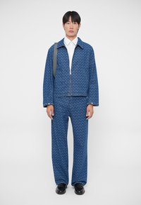 Chaqueta azul con estampado y pantalones a juego, hechos de una tela similar al denim. Presenta un cierre con cremallera, un cuello ancho y perneras de corte recto.