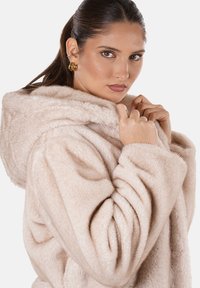 Felpa oversize in finta pelliccia beige chiaro con cappuccio, caratterizzata da una texture morbida e dettagli arricciati sulle maniche e sul davanti.