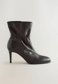 Tumepruun nahast keskpikk saabas, millel on terav varvas ja kitsas kõrge konts, kus on ümber pahkluude gathered elastne detail.