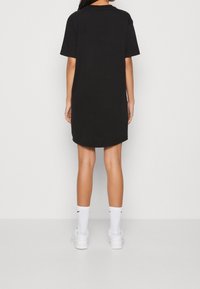 Czarna sukienka t-shirtowa z krótkimi rękawami, o luźnym kroju, gładkiej fakturze i sięgająca kolan, noszona z białymi skarpetkami i trampkami.