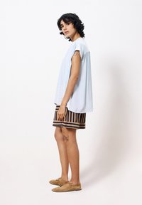 Lichtblauw bloesje met korte mouwen, losse pasvorm. Gecombineerd met gestreepte shorts in marineblauw en beige. Tan suède schoenen, eenvoudig ontwerp.