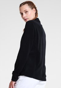 Svart långärmad topp med ställbar krage, tillverkad av mjukt tyg. Har en sömlös design, åtsittande stil och en slät textur.